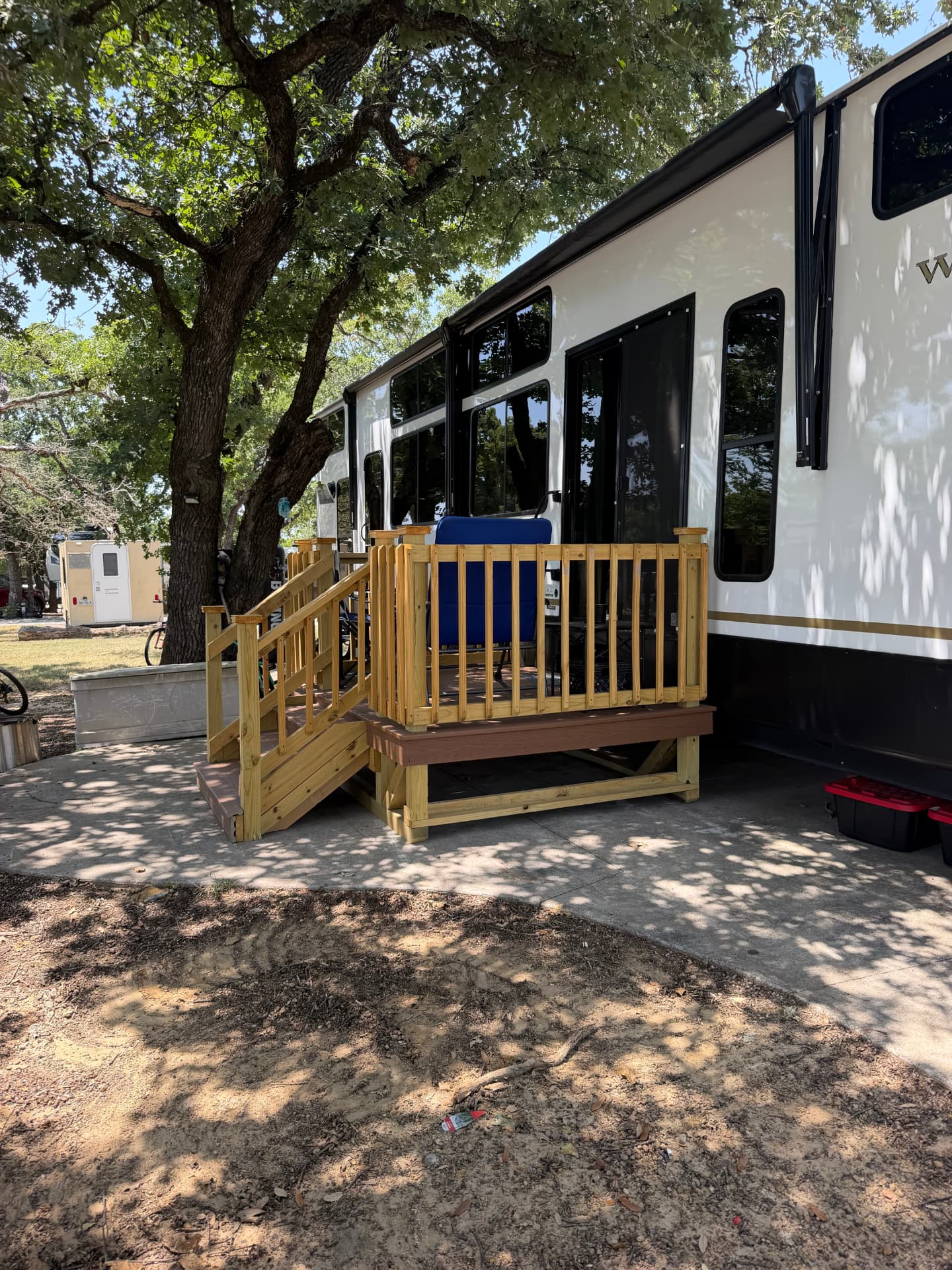 Small treated wood RV deck with steps and railing beside a travel trailer