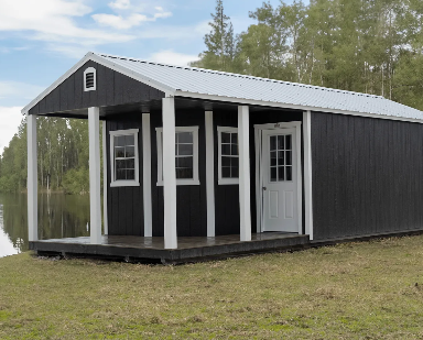 Black storage shed cabin with white porch posts and full-length covered porch