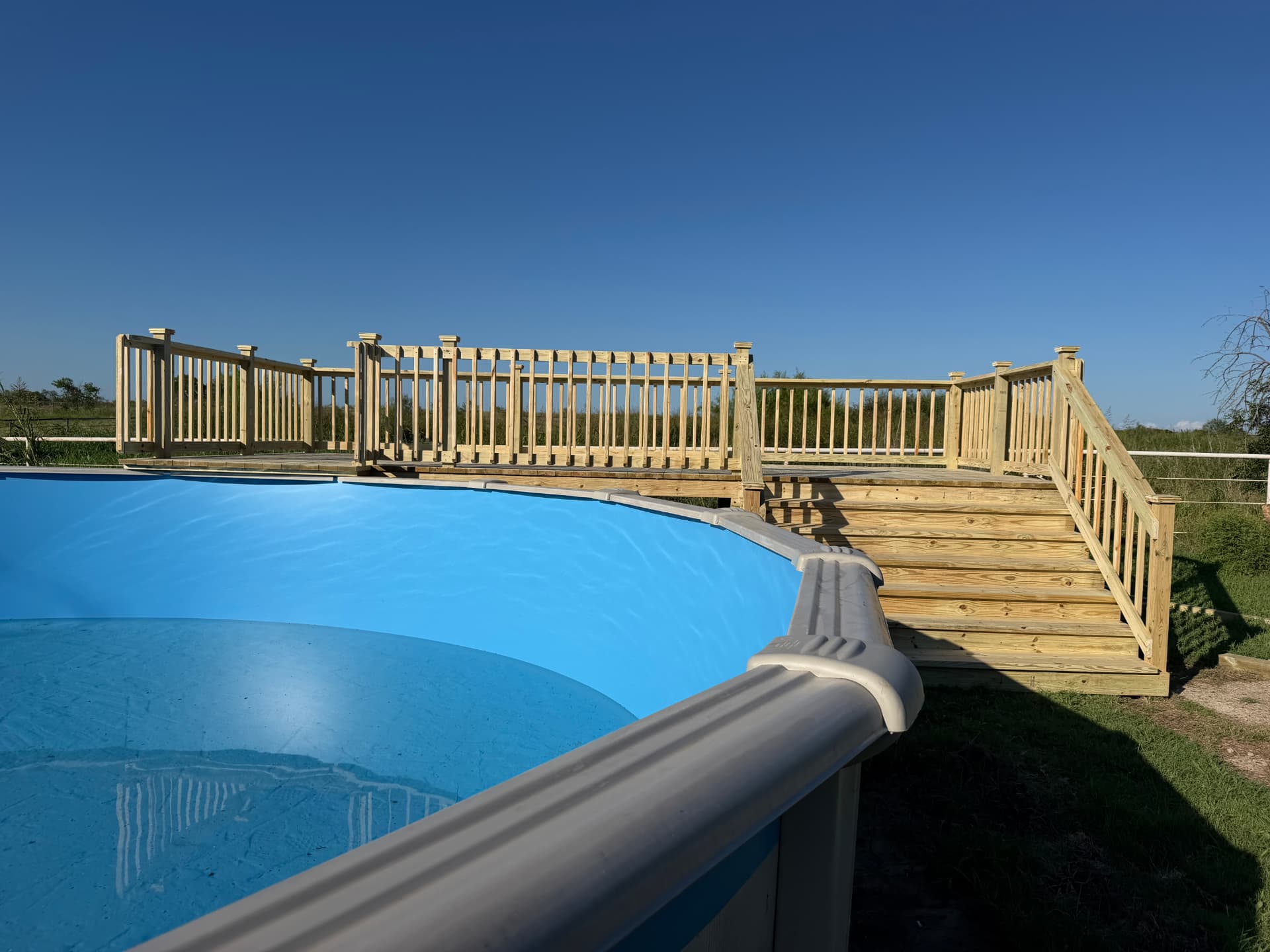 Long treated pool deck with railing and wide steps under a blue sky