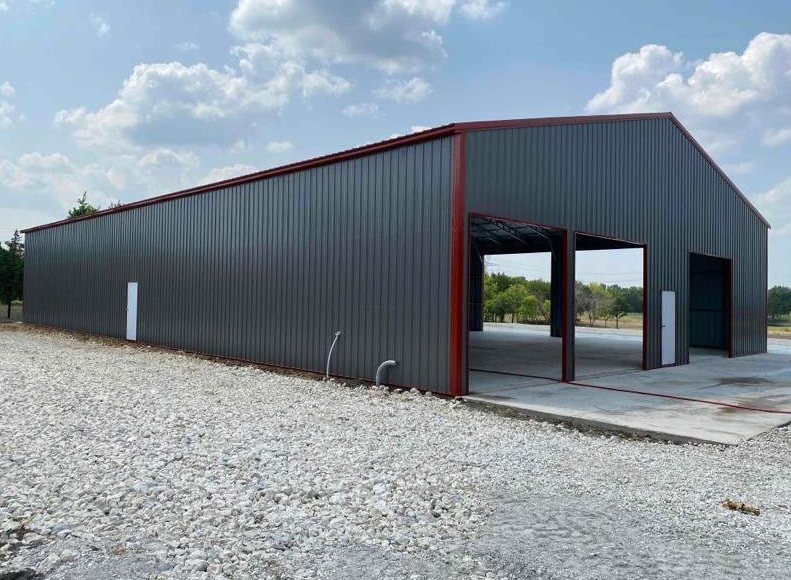 Large charcoal gray metal shop building with red trim and open bay doors