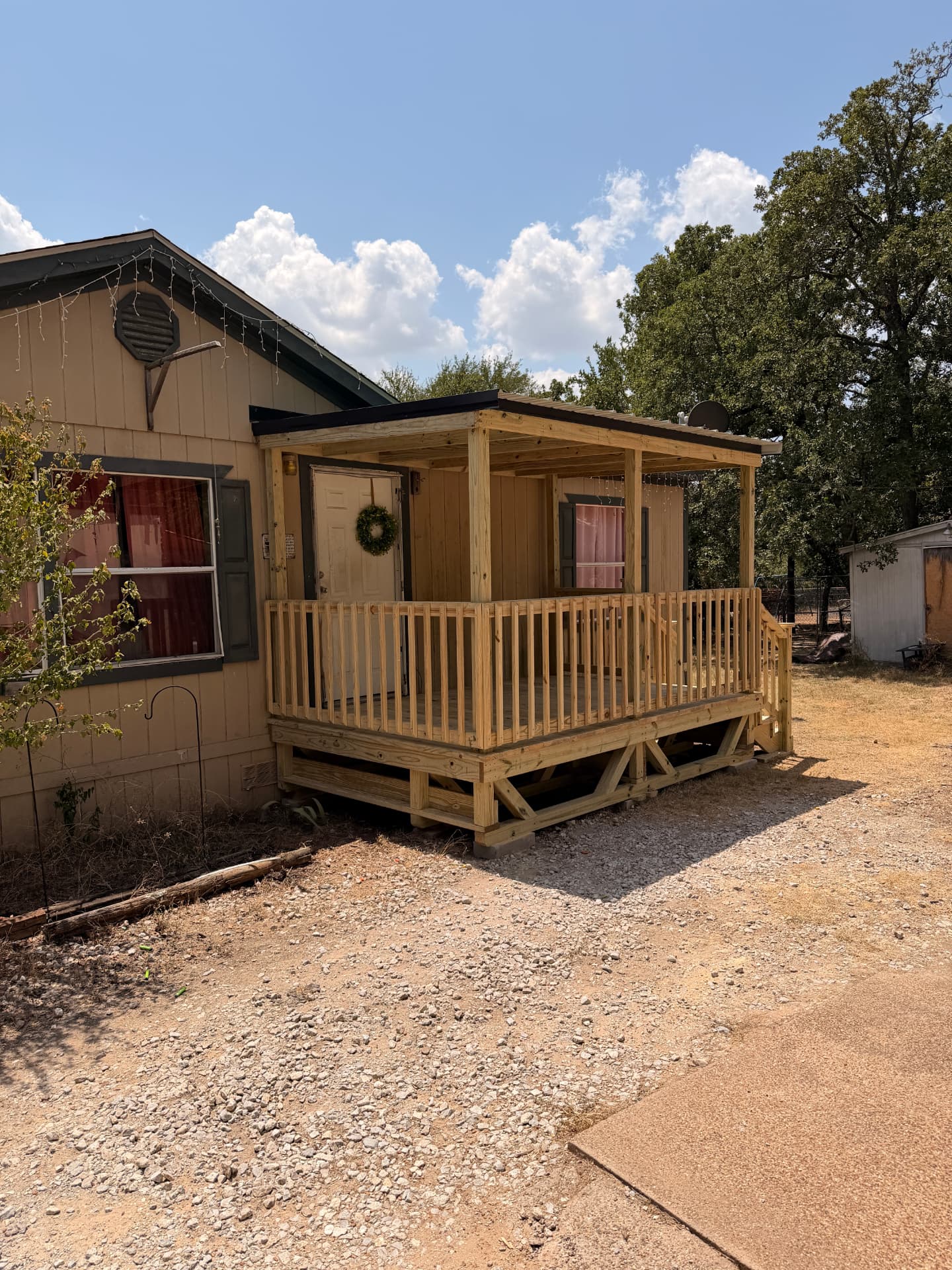 Covered treated wood porch deck with railing built onto a house
