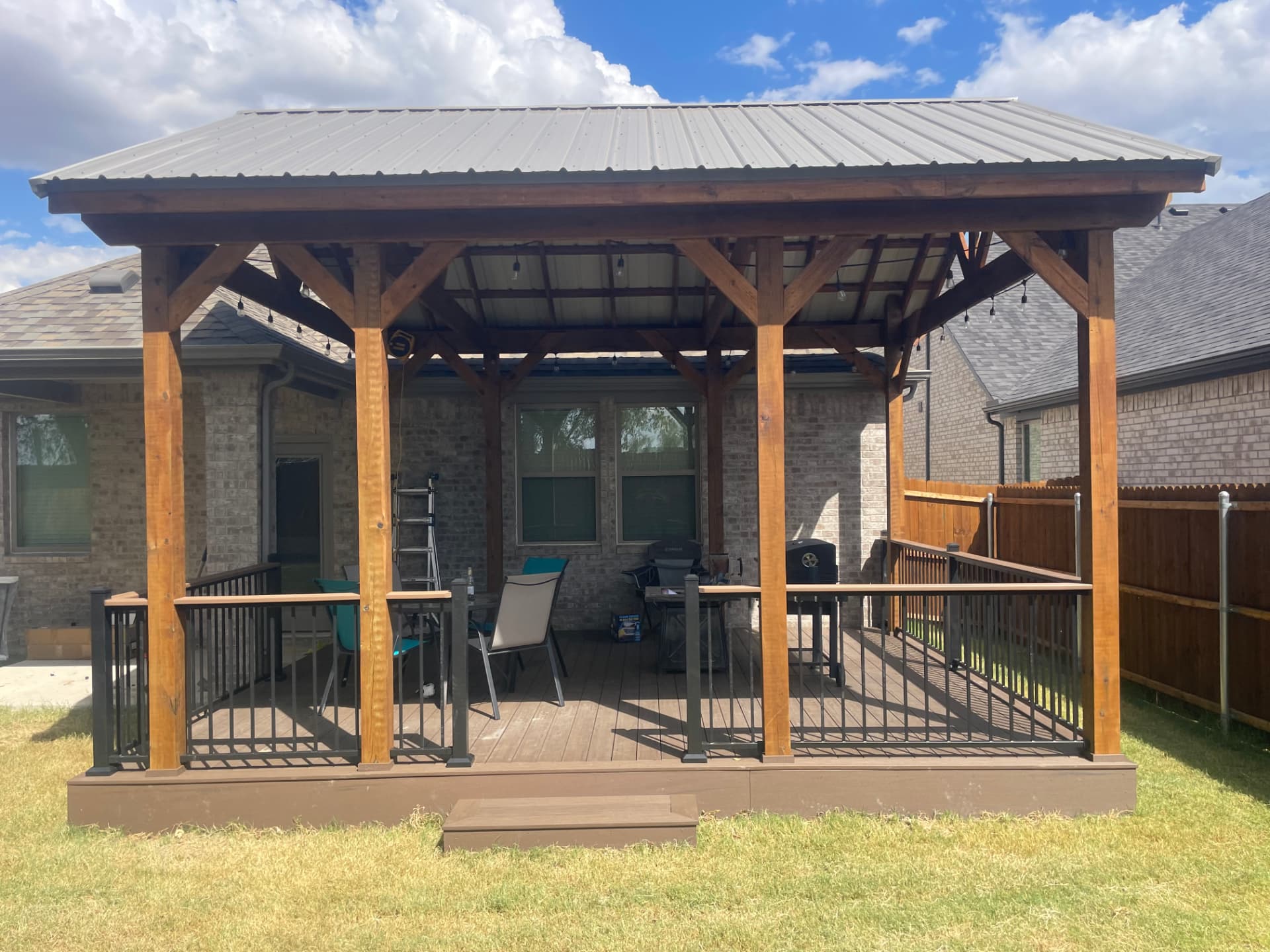 Cedar post covered patio with metal roof over a composite deck with black railing
