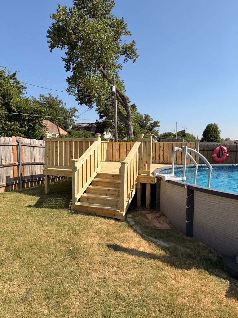Treated wood pool deck with privacy wall and stairs beside an above ground pool