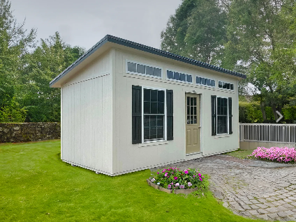 White storage shed with black shutters, transom windows, and a slant roof