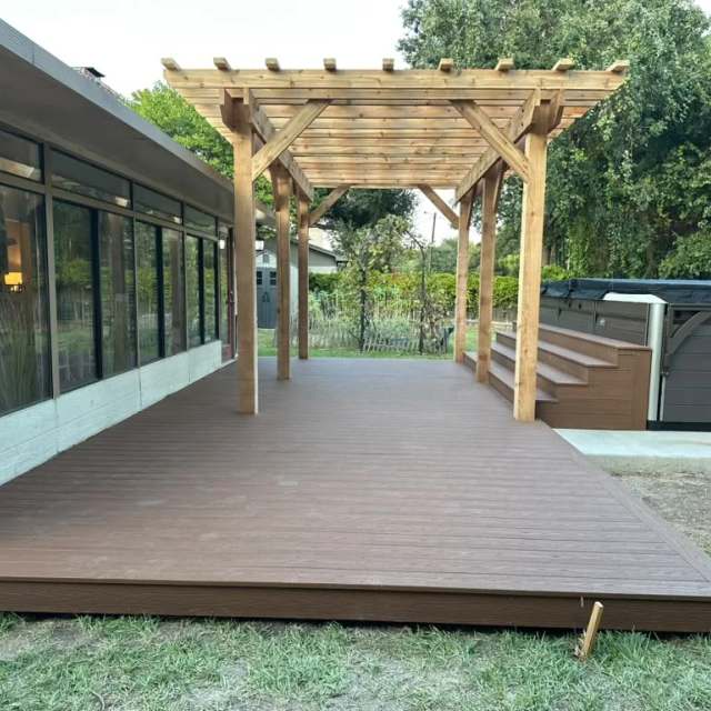 Brown composite deck with cedar pergola beside a cabin