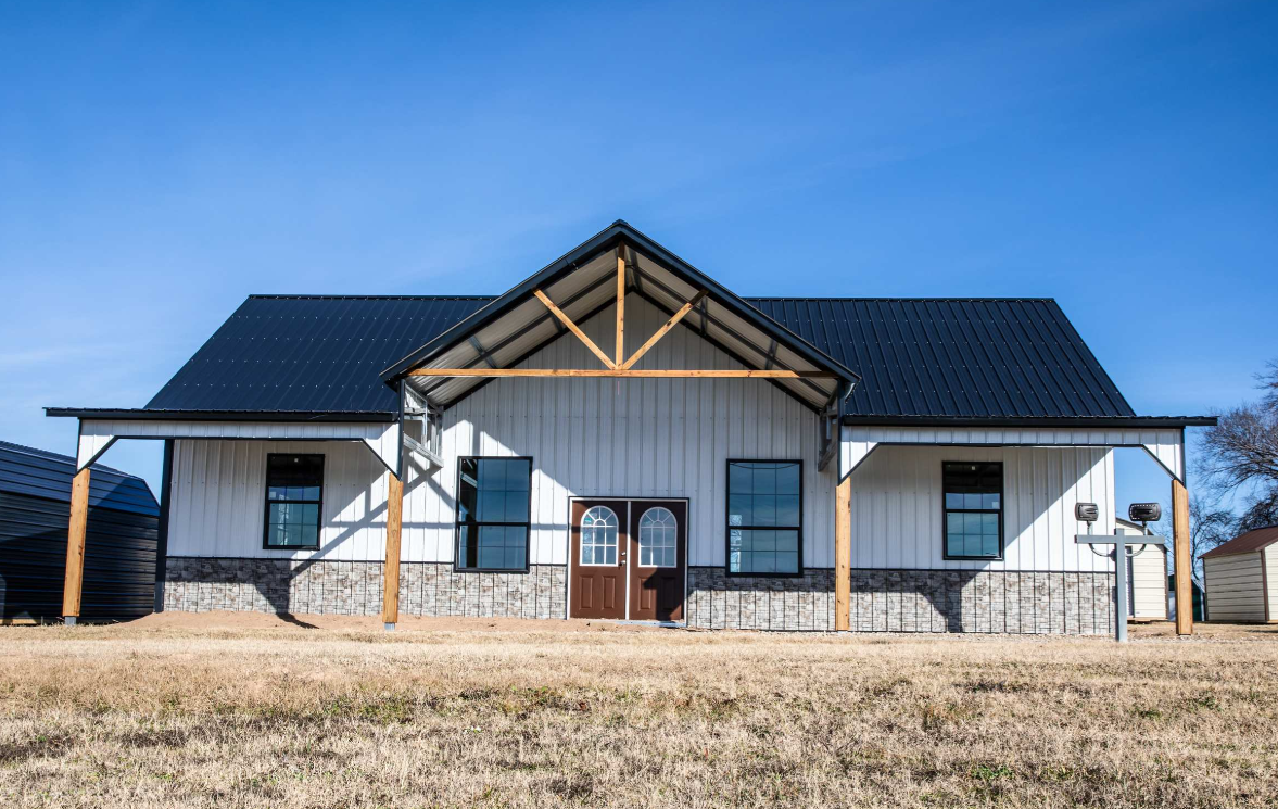 White metal barndominium with black roof, stone wainscot, and cedar porch posts