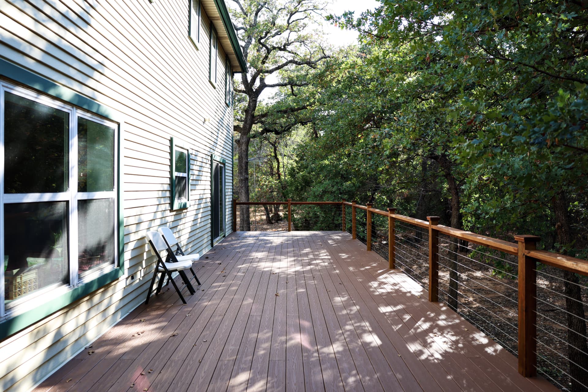 Long composite deck with cedar and cable railing beside a house in the trees