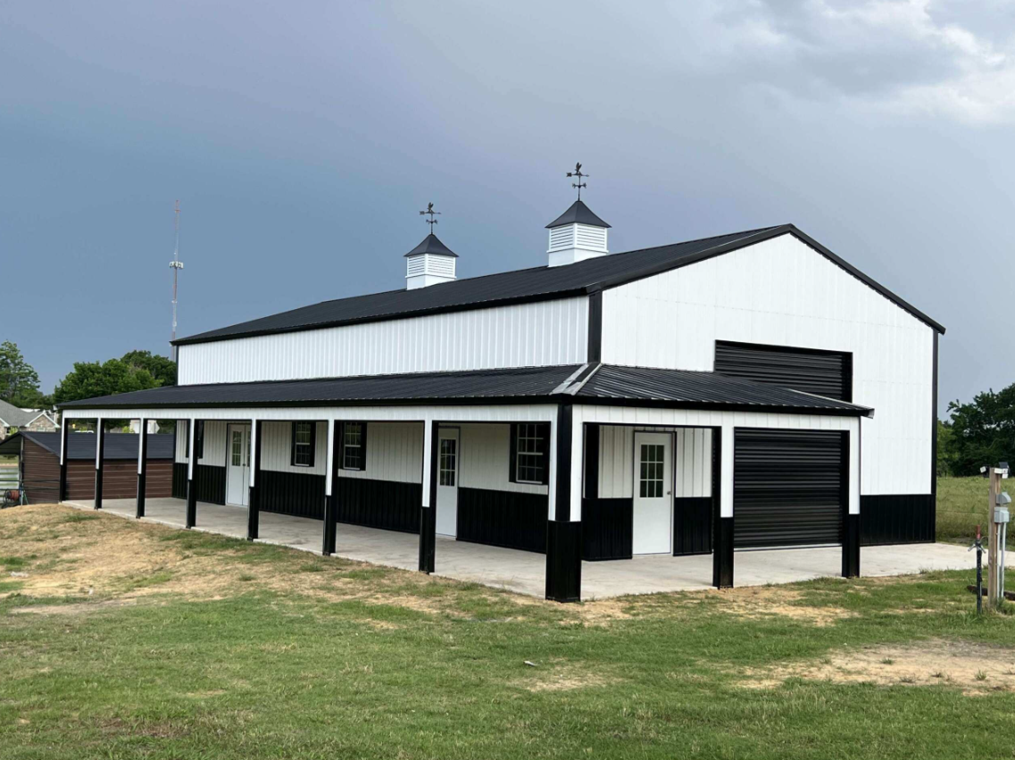 Black and white metal barn with covered porch, cupolas, and roll-up door