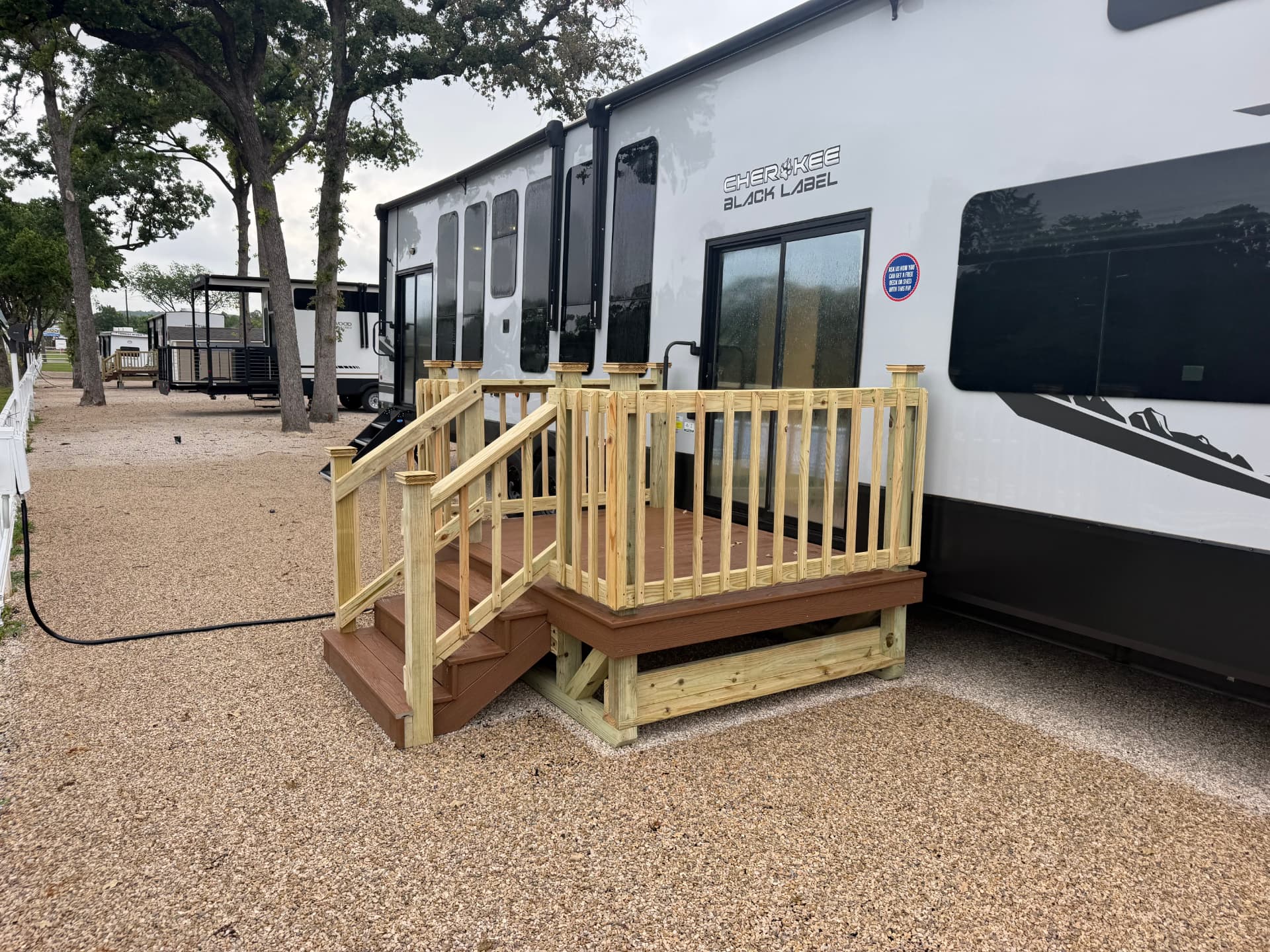 Composite RV deck with treated railing and steps beside a travel trailer